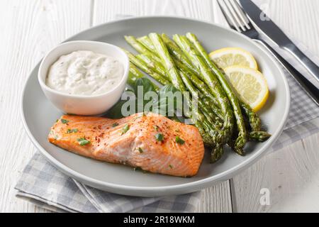 Delicious baked salmon with crispy asparagus served with tartar sauce close-up in a plate on the table. Horizontal Stock Photo