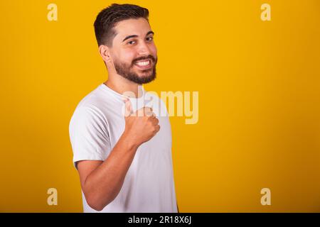 Brazilian Latin American man with thumb up, symbol of positive, approving, approved, cool, positivity, yellow background, space for text or advertisem Stock Photo