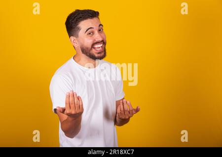 Brazilian Latin American man, with gesture calling, come, come, inviting, receiving, welcoming, happy, smiling, autruism, yellow background, space for Stock Photo