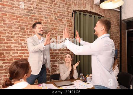 Happy office employees joining hands at work Stock Photo