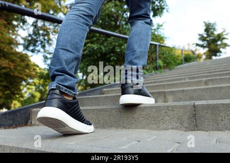 Man in stylish black sneakers walking up stairs, closeup Stock Photo