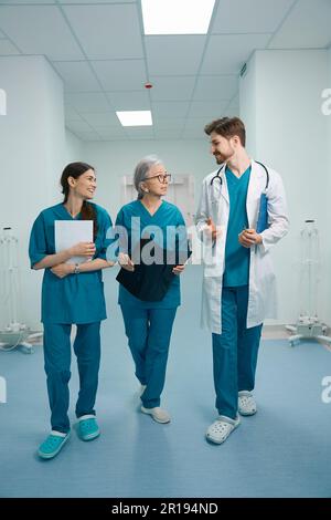 Man and two women in medical uniforms walk along hospital corridor Stock Photo
