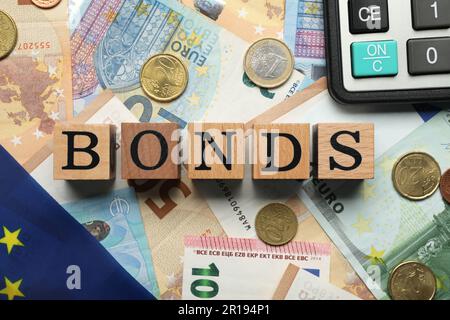 Wooden cubes with word Bonds, coins and calculator on euro banknotes, flat lay Stock Photo