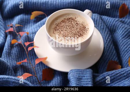 Cup of hot drink and leaves on blue knitted sweater. Cozy autumn atmosphere Stock Photo