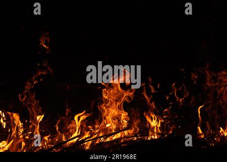 Burning red hot sparks fly from large fire in the night sky. Fire flames with sparks on the night black background Stock Photo