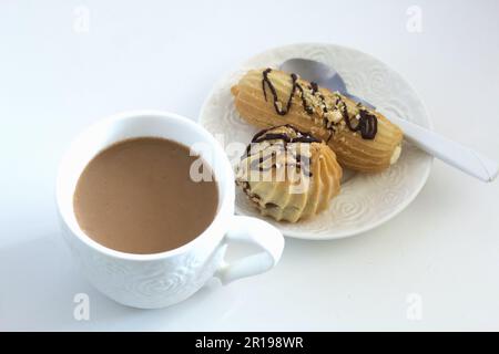 Eclairs on a saucer. A cup of coffee with milk. On a white tabletop. Stock Photo