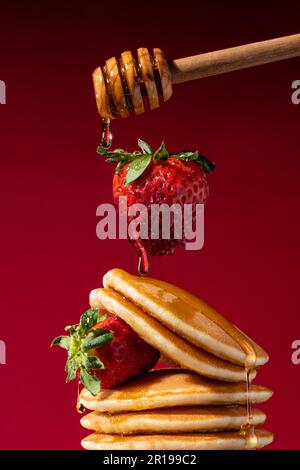 Levitating strawberry over a stack of pancakes drizzled with honey. Conceptual shot. Stock Photo