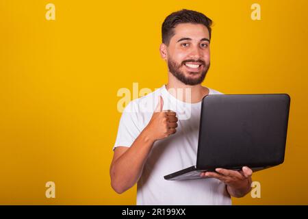 Brazilian Latin American man, happy, holding notebook and smiling, with thumb up, concept of work, approval, optimism, technology, internet access. Stock Photo