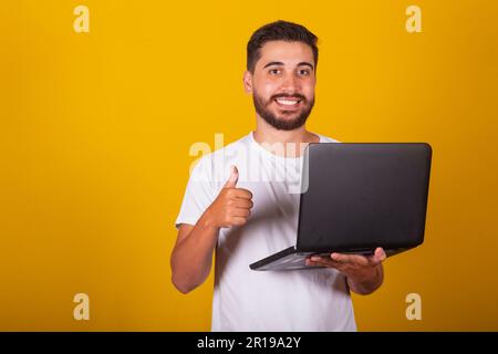 Brazilian Latin American man, happy, holding notebook and smiling, with thumb up, concept of work, approval, optimism, technology, internet access. Stock Photo