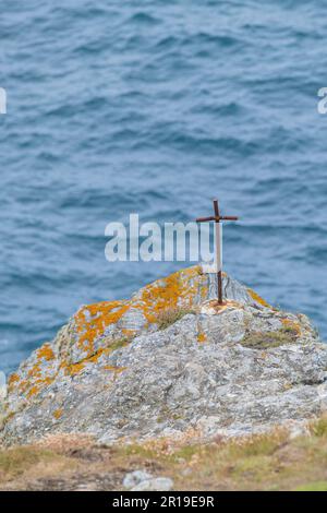 A small crude rusty iron cross cemented on rocks overlooking the sea on Pentire Point East in Newquay in Cornwall in England in the UK. Stock Photo