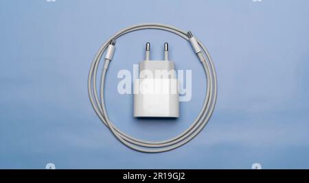 Mobile phone charger with cable wrapped next to it on blue background Stock Photo