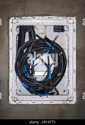 White plastic cables box with black wires installed on new gray wall at construction site Stock Photo