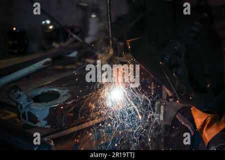 Welding old metal car part at workshop, sparks and smoke flying around, closeup detail Stock Photo