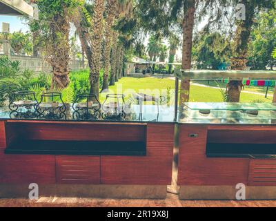 hotel area in a hot, tropical country. dining room for tourists. dishes are under a metal plate on the stand. near high, green palm trees. Stock Photo