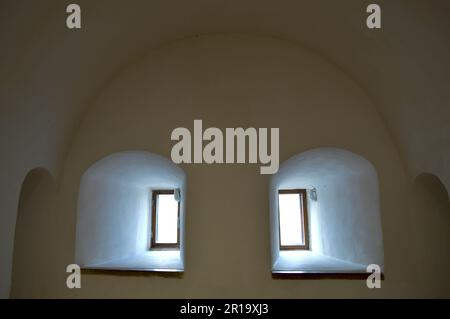 Small narrow windows with an arch on an old ancient stone thick wall in the basement, an old castle. The background. Stock Photo