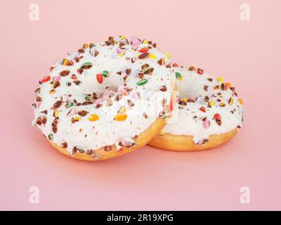 Two circle donut with white icing and choclate rainbow sprinkles on a trendy pink background. Tasty doughnutdonut, vertical view. Sweet food Stock Photo