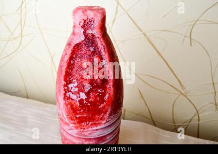 Frozen, tasty, red grated strawberry. Frozen bright berries in the form of a bottle in a cut on a beige background. Stock Photo
