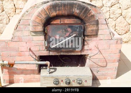 A large professional industrial brown stone oven grill oven with a tube for cooking frying food from a stone tiled on a stone wall background in the o Stock Photo