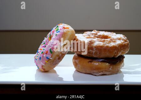 three Donuts on white plate close-up pink covered with chocolate And icing appetizing dessert laid out sprinkled with powder background for restaurant menu  Stock Photo
