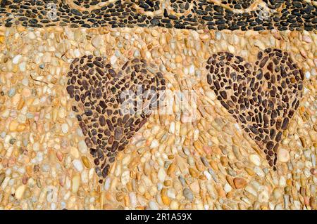 The texture of the stone wall, the road from small round and oval stones with abstracted lines of patterns of two hearts sandy seams of natural old ye Stock Photo