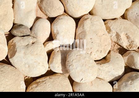 Texture of a stone wall, roads from large round and oval stones with sand with seams of natural old yellow black brown. The background. Stock Photo