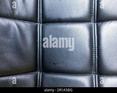 Texture of a relief surface made of black leather, artificial and artificial leather with a pattern of squares sewn with thread seams. The background. Stock Photo