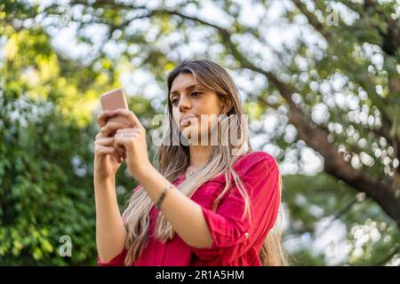 Low angle view of young blond woman using smartphone outdoors.  Modern technologies concept Stock Photo