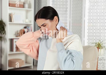 Young woman using heating pad on neck at home Stock Photo