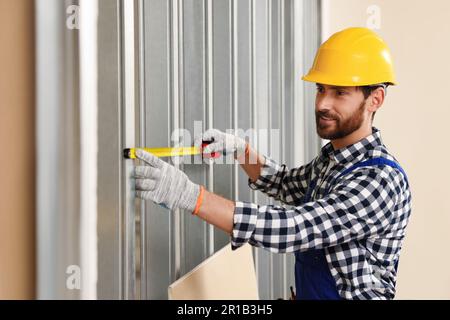 Professional builder in uniform working with measuring tape indoors Stock Photo