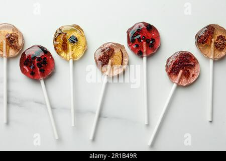 Sweet colorful lollipops with berries on white marble table, flat lay Stock Photo