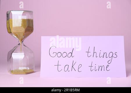 Card with phrase Good Things Take Time and sand clock on pink background. Motivational quote Stock Photo