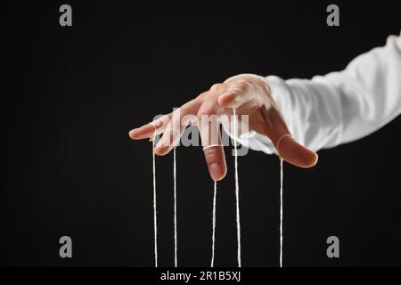 Woman pulling strings of puppet on black background, closeup Stock Photo