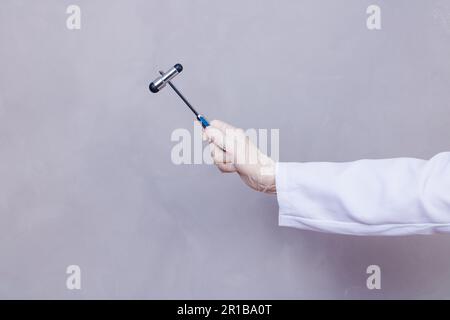 The doctor is holding a neurological hammer on a grey background. The neurologist checks the patient's reflexes with a hammer. Diagnostics, healthcare Stock Photo