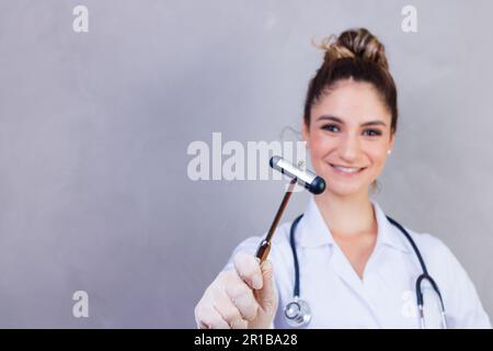The doctor is holding a neurological hammer on a grey background. The neurologist checks the patient's reflexes with a hammer. Diagnostics, healthcare Stock Photo