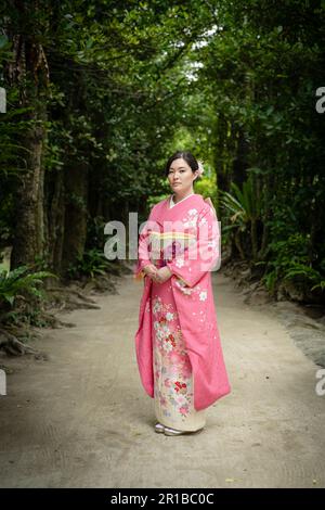 Beautiful young mixed race Japanese / American woman wearing a kimono standing on the footpath of Bise Village, Motobu Town, Okinawa, Japan. Stock Photo