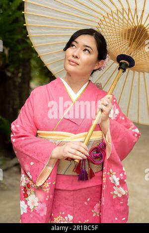Beautiful young mixed race Japanese / American woman wearing a kimono with wagasa (umbrella)  standing on the footpath of Bise Village, Motobu Town, Okinawa, Japan. Stock Photo