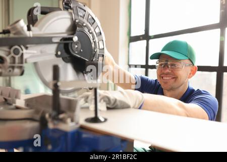 Smiling employee cuts wooden board with sawing machine Stock Photo