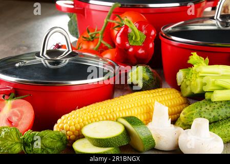 Composition with red steel pots and variety of fresh vegetables Stock Photo