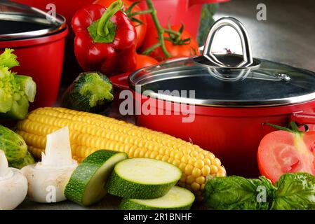 Composition with red steel pots and variety of fresh vegetables Stock Photo