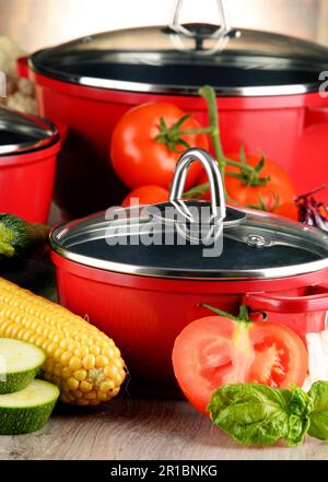 Composition with red steel pots and variety of fresh vegetables Stock Photo