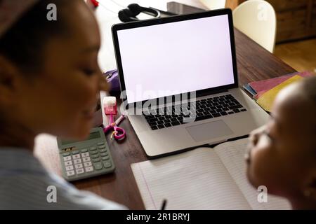 African american mother helping daughter with schoolwork using laptop at home, copy space on screen Stock Photo