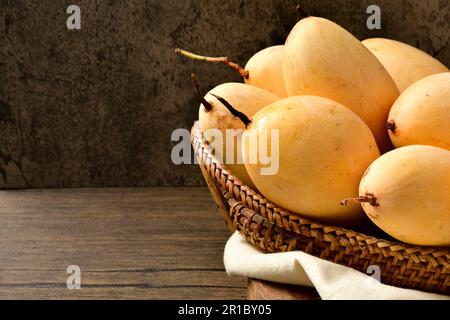 Thai mangos in wicker baskets on wooden table and dark background.Horizontal.Copy space.Copy text.Yellow Mangoes in baskets.mango nam dok mai. Stock Photo