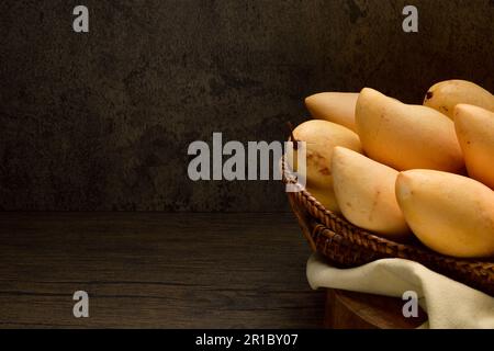 Thai mangos in wicker baskets on wooden table and dark background.Horizontal.Copy space.Copy text.Yellow Mangoes in baskets.mango nam dok mai. Stock Photo