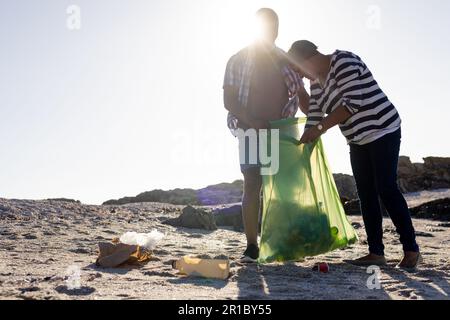 Happy senior african american couple with bag picking waste at beach Stock Photo