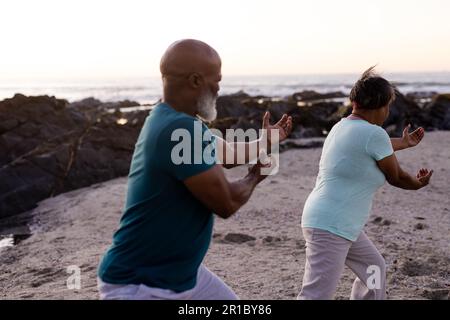 Focused senior african american couple practicing yoga and doing poses at beach Stock Photo