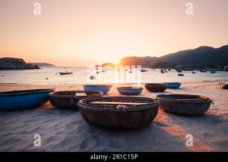 Basket boats on sand beach in bay against sea at beautiful sunset. Fishing village on Cham Islands in Vietnam. Stock Photo