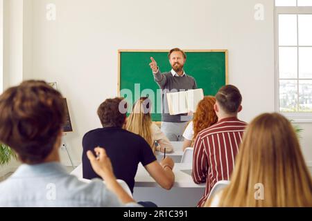 Middle aged professor lector is showing on student in class for answer the question. Stock Photo