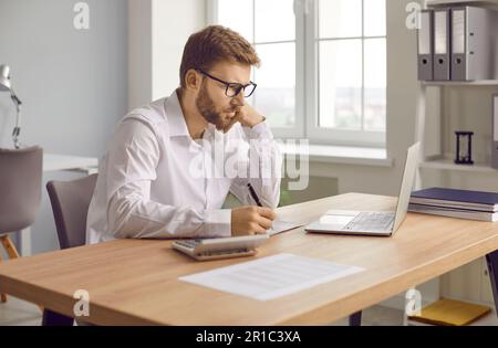 Focused businessman sitting at laptop computer and writing notes Stock Photo