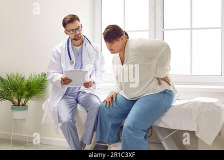 Fat young sitting at dwoman sitting in the doctor's office suffering from backache. Stock Photo