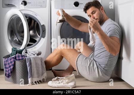 Man with clothes near washing machine. Laundry cleaning. Housework, homework, male housekeeper. Husband man doing laundry at home. Washer and dryer at Stock Photo